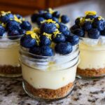 Three individual Lemon Blueberry Cheesecake Jars layered with graham cracker crust, creamy filling, whipped topping, blueberries, and lemon zest.