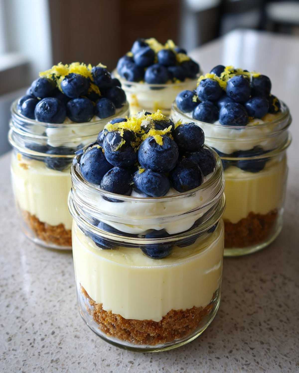 Four individual Lemon Blueberry Cheesecake Jars with graham cracker crust, creamy filling, topped with fresh blueberries and lemon zest.