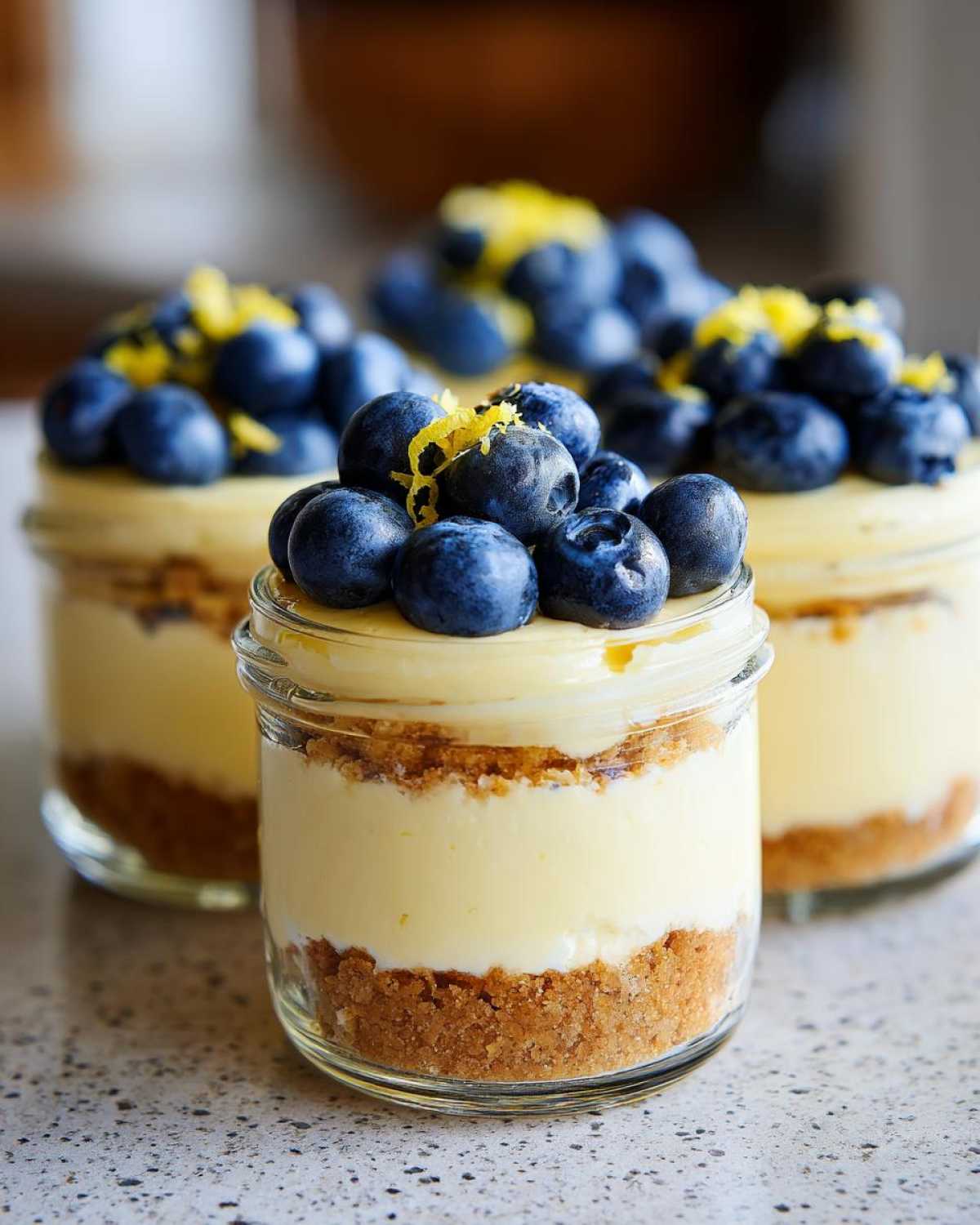 Close-up of layered Lemon Blueberry Cheesecake Jars topped with fresh blueberries and lemon zest.