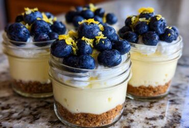 Three individual Lemon Blueberry Cheesecake Jars layered with graham cracker crust, creamy filling, whipped topping, blueberries, and lemon zest.