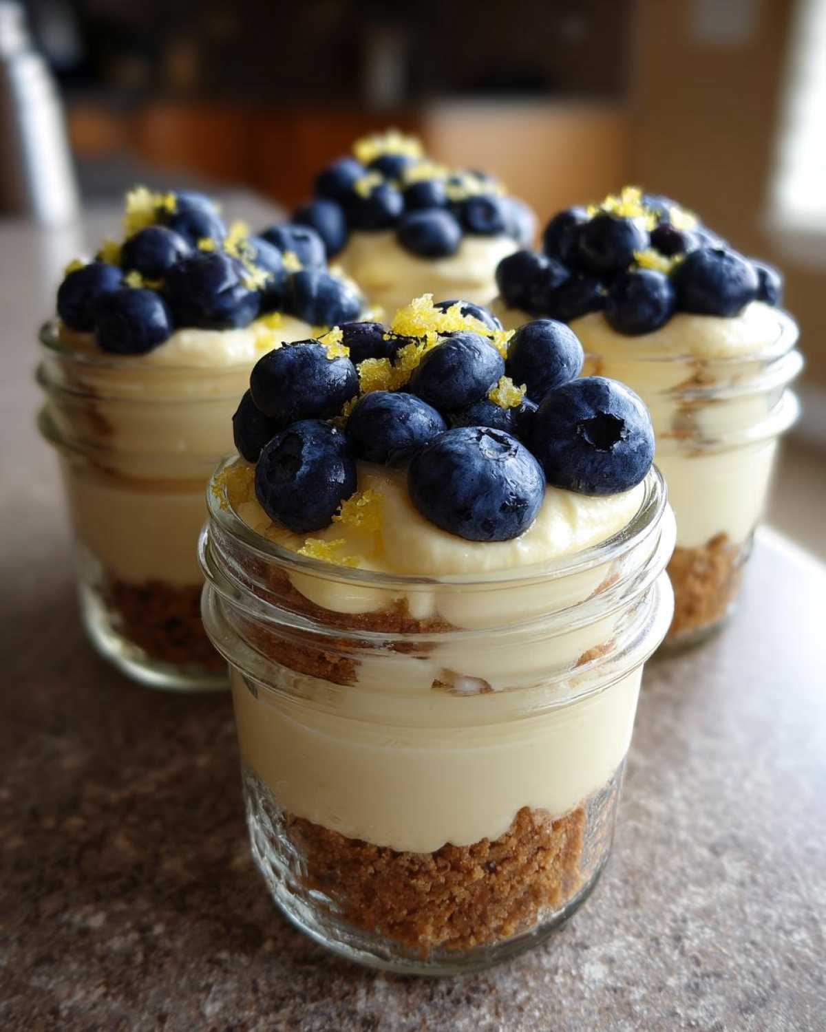Four individual Lemon Blueberry Cheesecake Jars layered with graham cracker crust, creamy filling, topped with fresh blueberries and lemon zest.