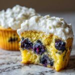 Close-up of a Lemon Blueberry Cupcakes cut in half showing moist yellow cake and burst blueberries under cream cheese frosting.