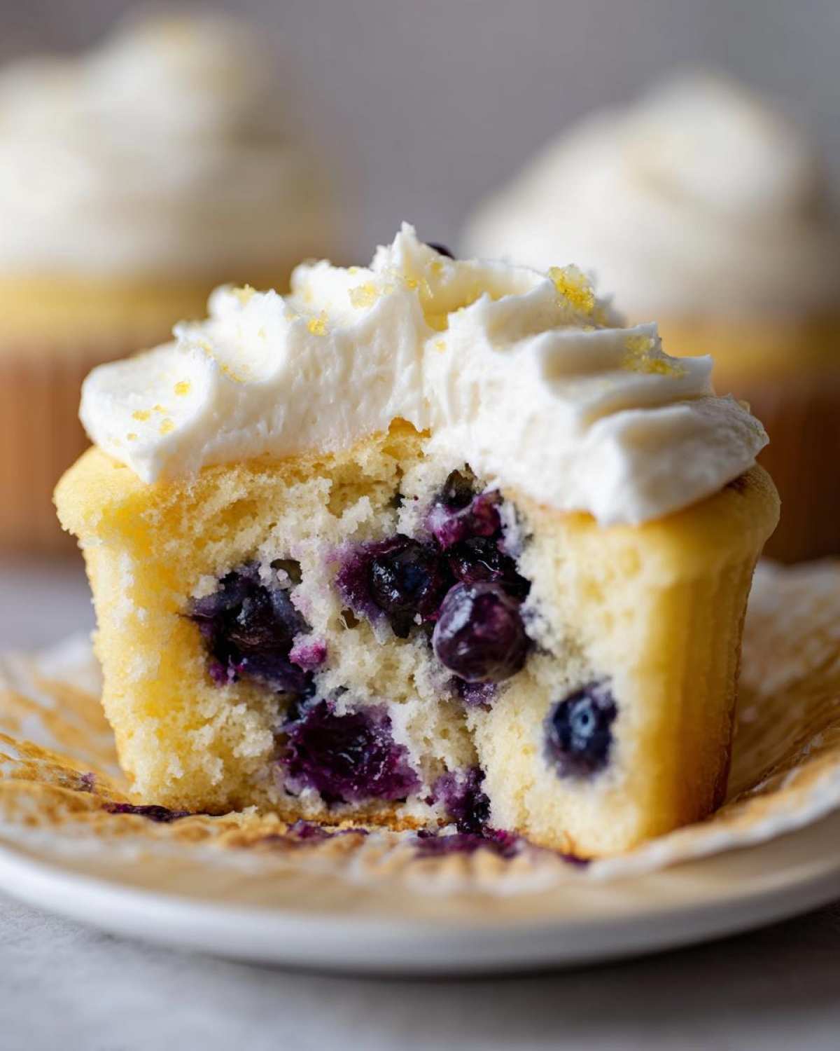 Close-up of a Lemon Blueberry Cupcakes cut in half showing moist cake, blueberries, and cream cheese frosting.