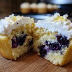 A Lemon Blueberry Cupcake cut in half showing moist cake, blueberries, and cream cheese frosting.