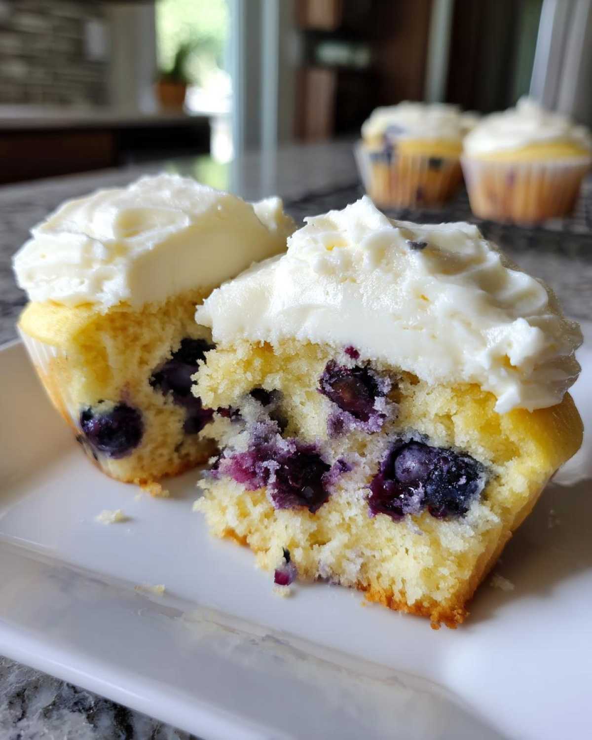 Close-up of a Lemon Blueberry Cupcakes with Cream Cheese Frosting cut in half, showing moist cake and blueberries.