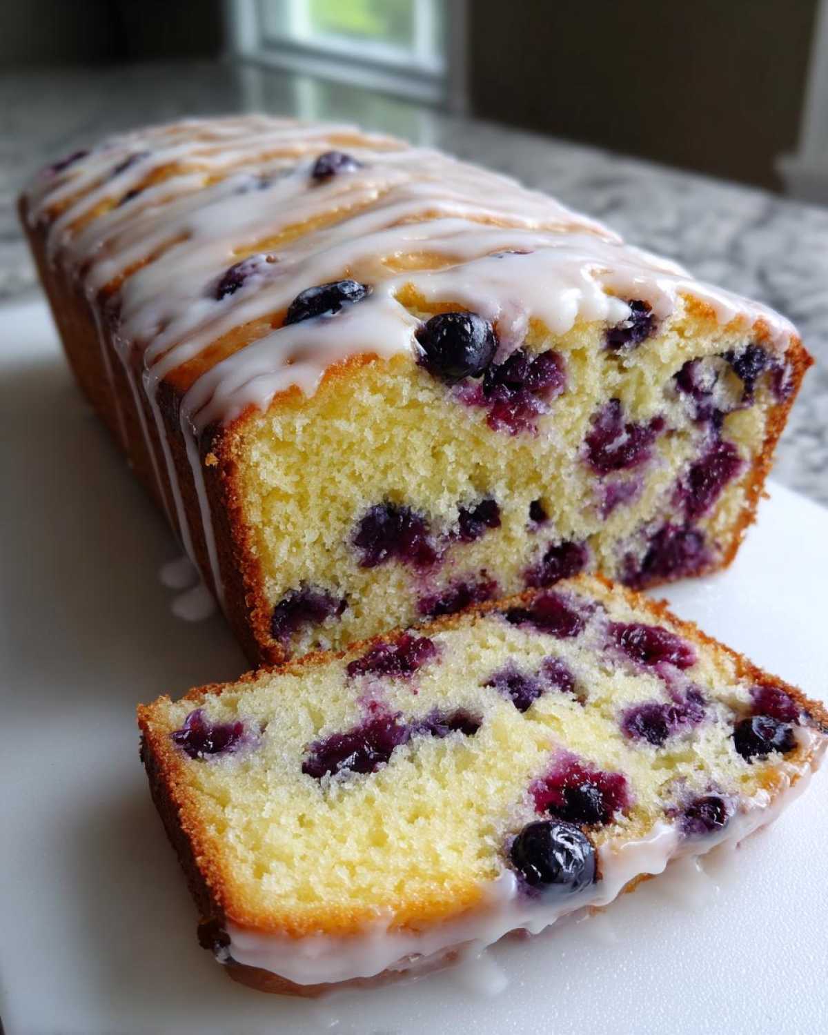 A slice cut from a Lemon Blueberry Yogurt Loaf, showing moist crumb and blueberries, drizzled with white icing.