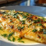 Close-up of a perfectly cooked Lemon Garlic Butter Tilapia fillet swimming in rich butter sauce and topped with fresh parsley.