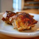 Close-up of crispy, golden-brown Lemon Garlic Roasted Chicken Thighs seasoned with herbs.