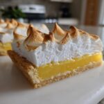 A close-up side view of a Lemon Meringue Pie Bars square showing the crust, bright yellow lemon filling, and toasted meringue peaks.
