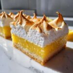 Close-up of a layered Lemon Meringue Pie Bars slice showing crust, bright yellow curd, and toasted meringue peaks.