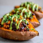 Close-up of Loaded Veggie Stuffed Sweet Potatoes topped with quinoa, black beans, and a bright green sauce.