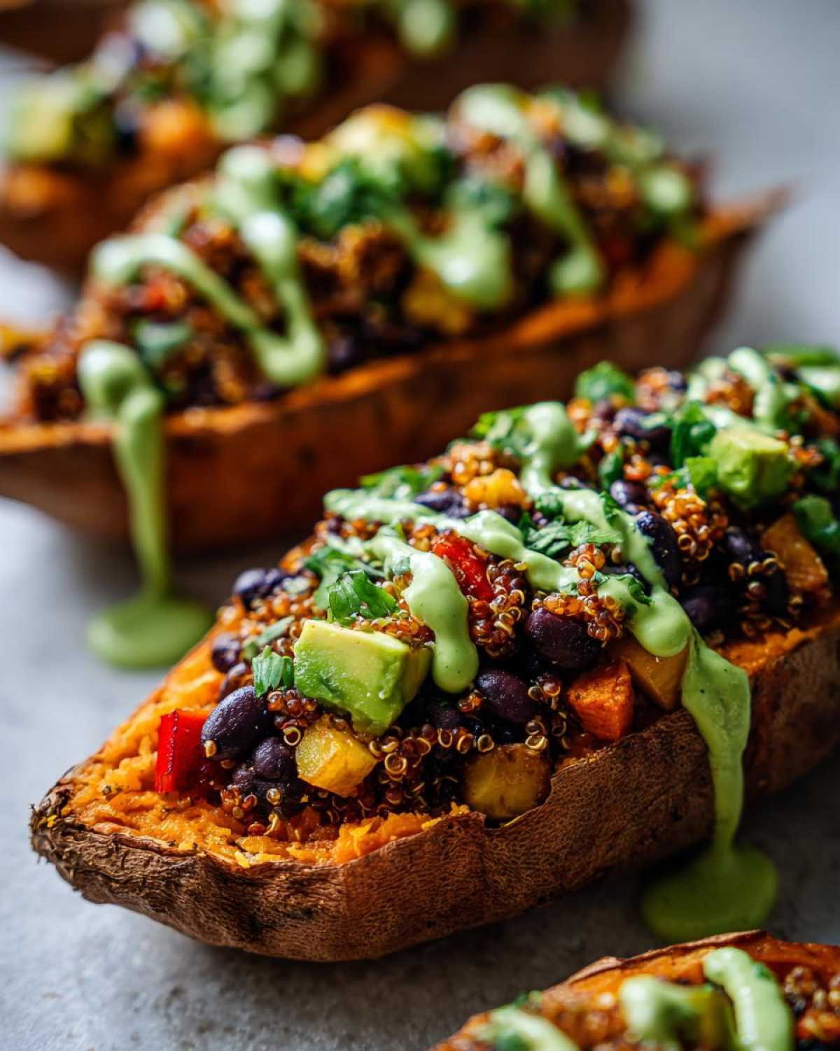 Close-up of Loaded Veggie Stuffed Sweet Potatoes topped with quinoa, black beans, avocado, and a bright green drizzle.