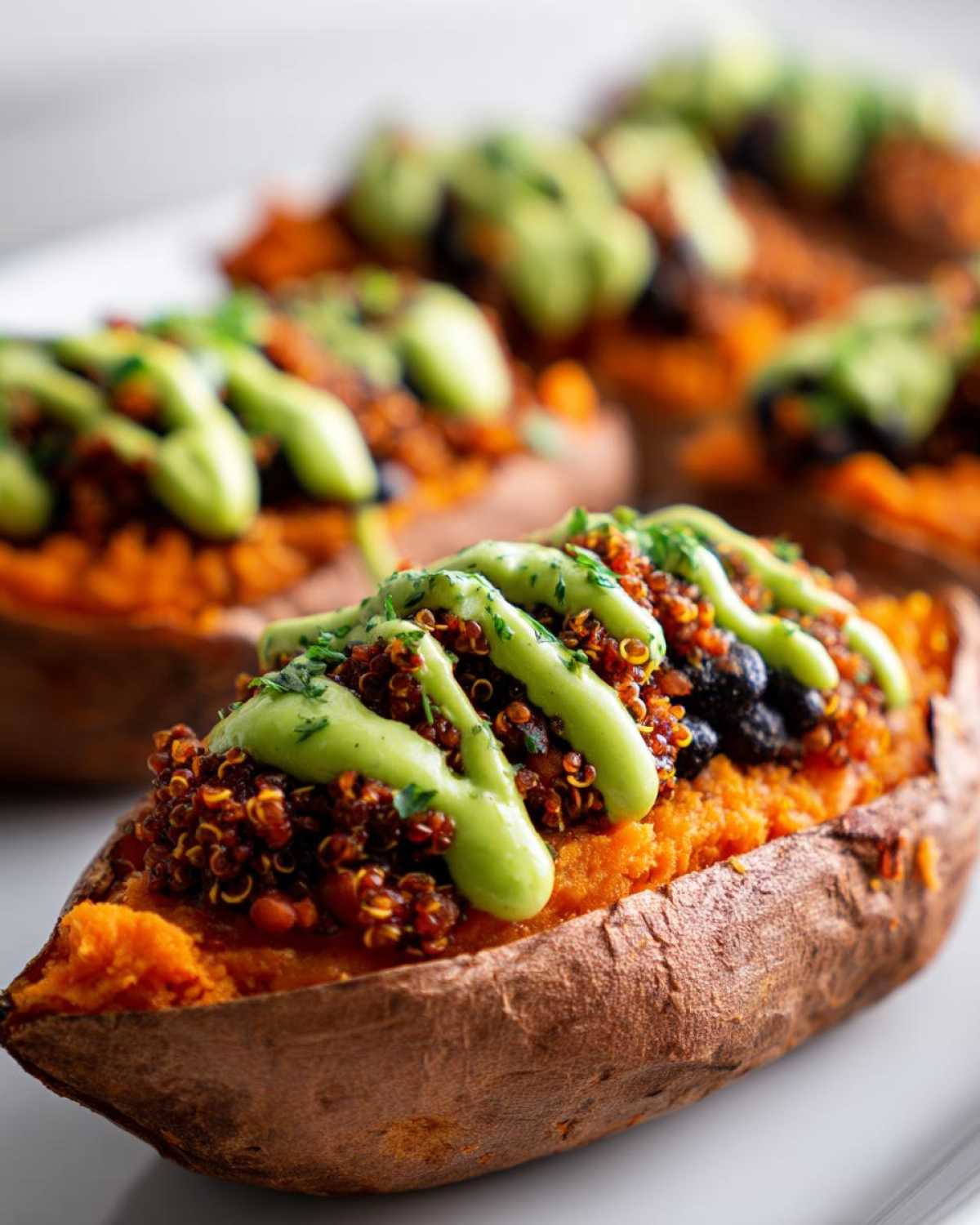 A close-up of one of the Loaded Veggie Stuffed Sweet Potatoes topped with quinoa, black beans, and a bright green sauce.