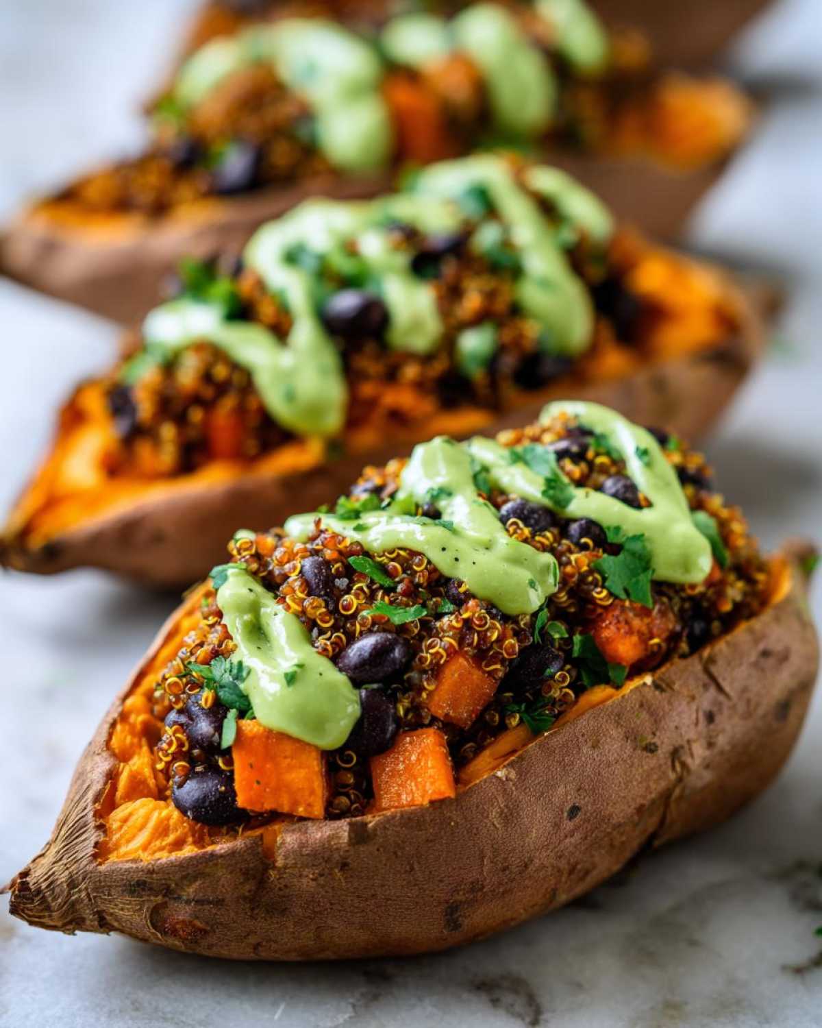 Close-up of Loaded Veggie Stuffed Sweet Potatoes filled with quinoa, black beans, and topped with a creamy green sauce.