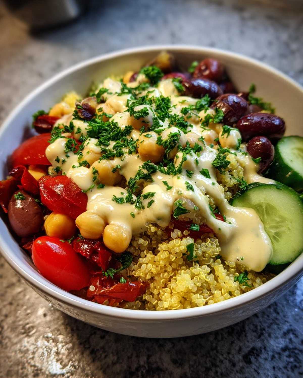 Close-up of a vibrant Mediterranean Quinoa Bowl with Lemon Tahini Sauce drizzled over chickpeas, tomatoes, and cucumbers.
