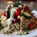 Close-up of a vibrant Mediterranean Quinoa Bowl topped with tomatoes, olives, cucumber, and drizzled with lemon tahini sauce.