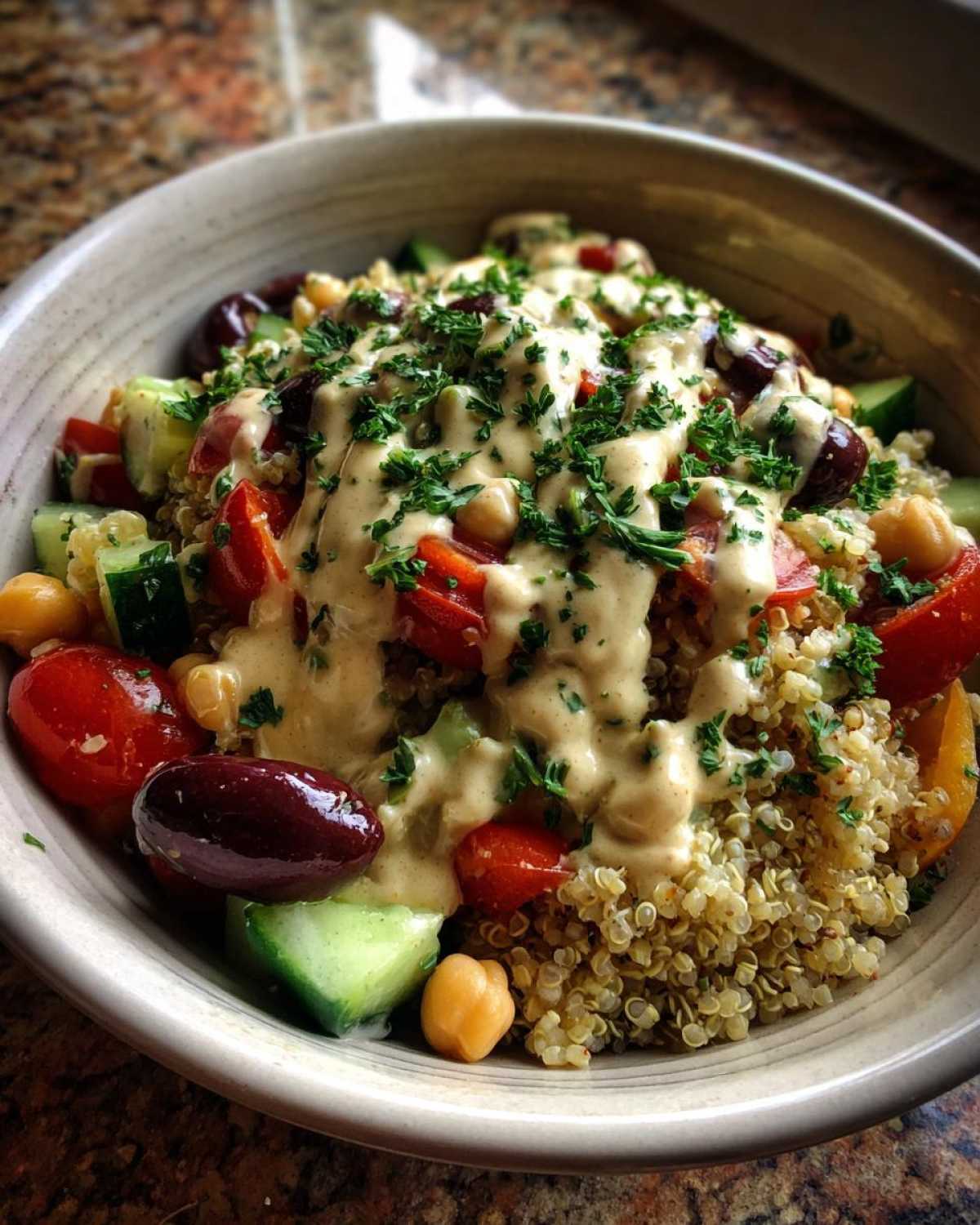 Close-up of a vibrant Mediterranean Quinoa Bowl with Lemon Tahini Sauce, topped with olives, tomatoes, and parsley.