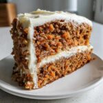 Close-up of a thick slice of Moist Carrot Cake with Cream Cheese Frosting showing visible shredded carrots.