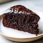 Close-up of a rich, dark slice of Gluten-Free Chocolate Cake topped with glossy chocolate ganache.
