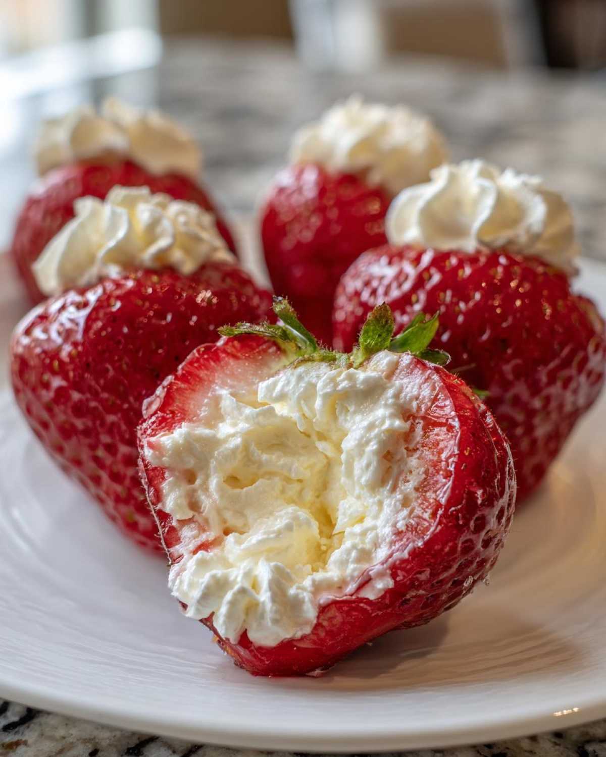 Close-up of fresh strawberries filled with creamy white no-bake cheesecake filling, served on a white plate.