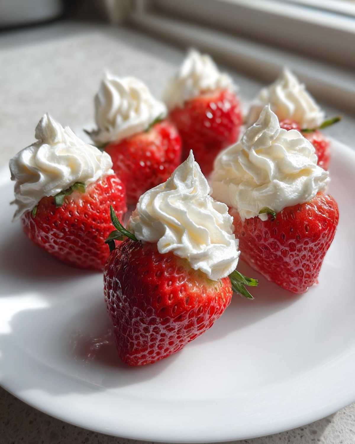Six bright red strawberries filled with creamy white no-bake cheesecake filling and topped with whipped cream.