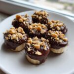 Close-up of several No-Bake Chocolate Covered Banana Bites topped with chopped peanuts on a white plate.