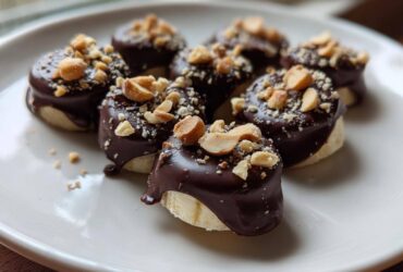 Close-up of several No-Bake Chocolate Covered Banana Bites topped with chopped peanuts on a white plate.