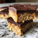 Two stacked squares of No-Bake Chocolate Peanut Butter Oat Bars showing the thick oat base and chocolate topping.