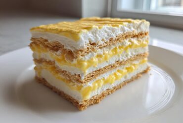 A layered slice of No-Bake Lemon Icebox Cake showing graham crackers, lemon curd, and whipped cream.