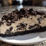 A rich slice of No-Bake Oreo Cheesecake showing the creamy filling mixed with cookie pieces on a white plate.