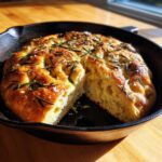 A golden, fluffy No-Knead Skillet Focaccia with Rosemary, cut open in a cast iron pan.