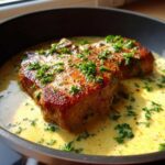 Two seared pork chops simmering in a rich, creamy garlic sauce and topped with fresh parsley.