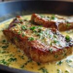 Close-up of seared pork chops simmering in a rich, creamy garlic sauce garnished with fresh parsley, perfect for One-Pan Creamy Garlic Pork Chops.