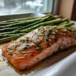 A perfectly cooked fillet of One-Pan Lemon Garlic Salmon topped with herbs, next to roasted asparagus spears.