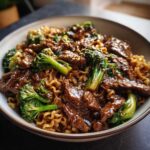 Close-up of One-Pot Beef and Broccoli Ramen Noodles coated in a glossy brown sauce, garnished with sesame seeds.