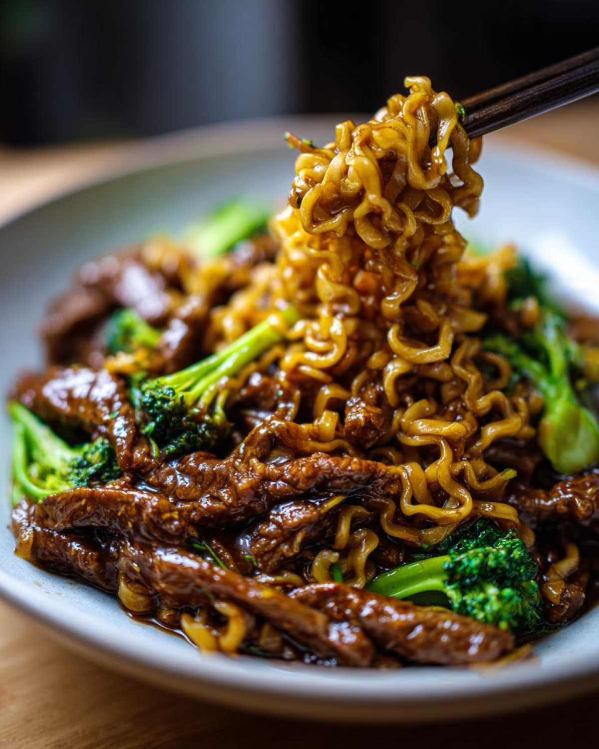 Chopsticks lifting glossy noodles from a bowl of One-Pot Beef and Broccoli Ramen Noodles with tender beef strips.