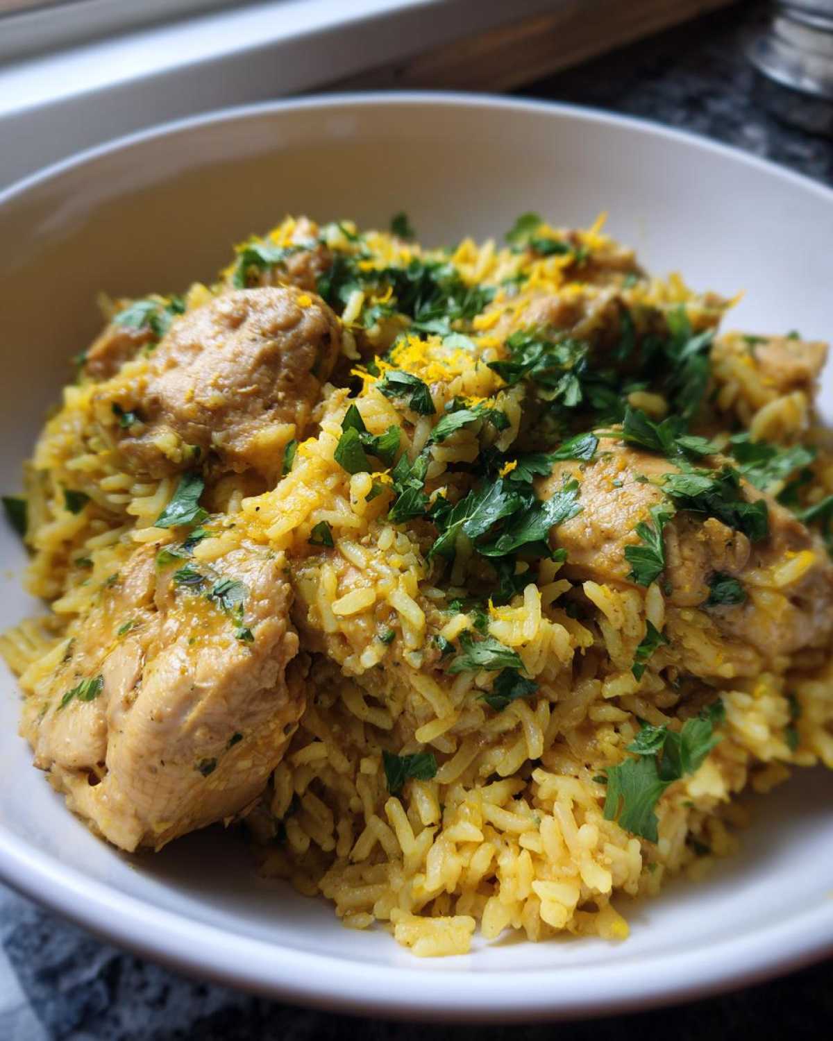A close-up of One-Pot Chicken and Rice with Lemon and Herbs, topped with fresh parsley and lemon zest.