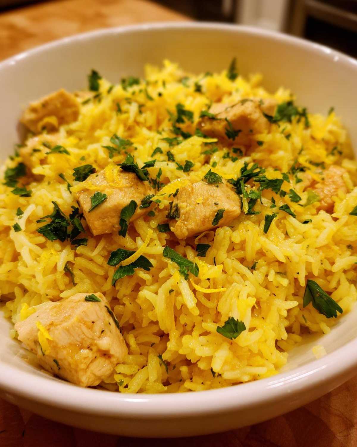 Close-up of a white bowl filled with bright yellow One-Pot Chicken and Rice with Lemon and Herbs, topped with fresh parsley.