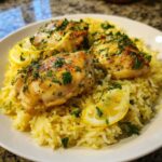 Three pieces of golden-brown chicken served over yellow rice, garnished with lemon slices and fresh parsley in One-Pot Chicken and Rice with Lemon and Herbs.