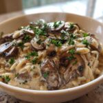 A close-up of a white bowl filled with One-Pot Creamy Mushroom Orzo, topped with sautéed mushrooms and fresh parsley.