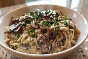 A close-up of a white bowl filled with One-Pot Creamy Mushroom Orzo, topped with sautéed mushrooms and fresh parsley.
