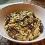 Close-up of a white bowl filled with One-Pot Creamy Mushroom Orzo topped with sautéed mushrooms and parsley.