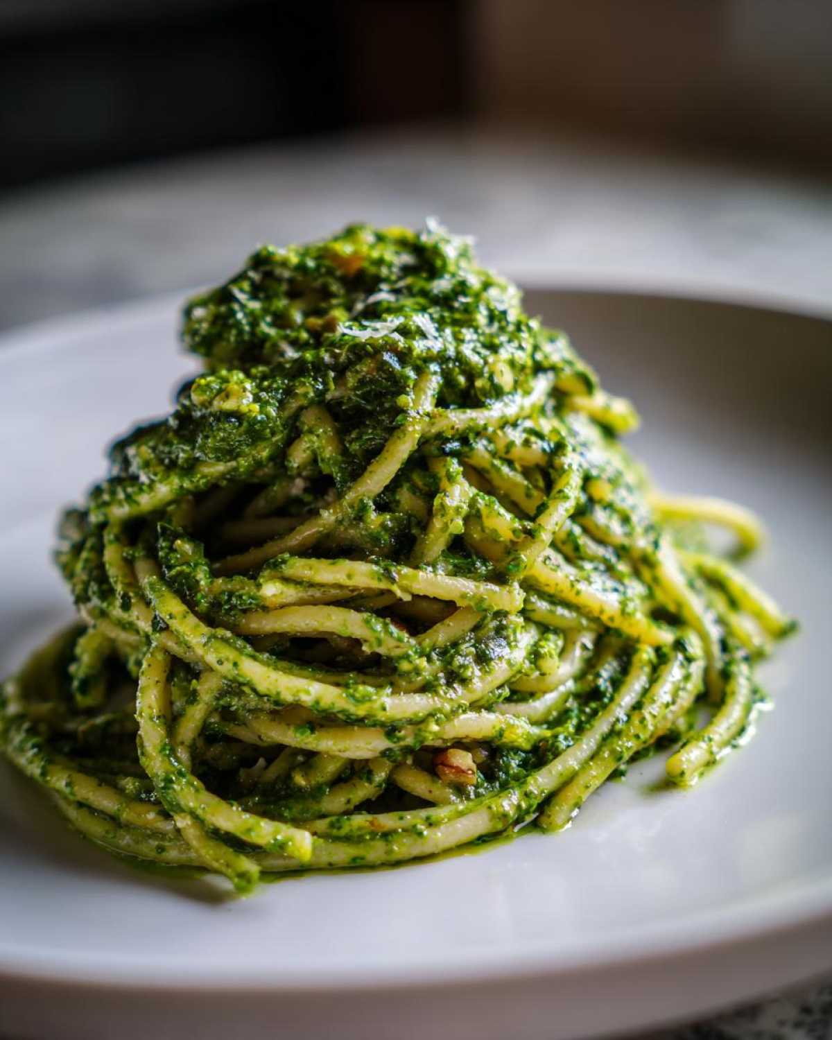 Close-up of spaghetti tossed generously with bright green Vegan Basil Pesto, served on a white plate.