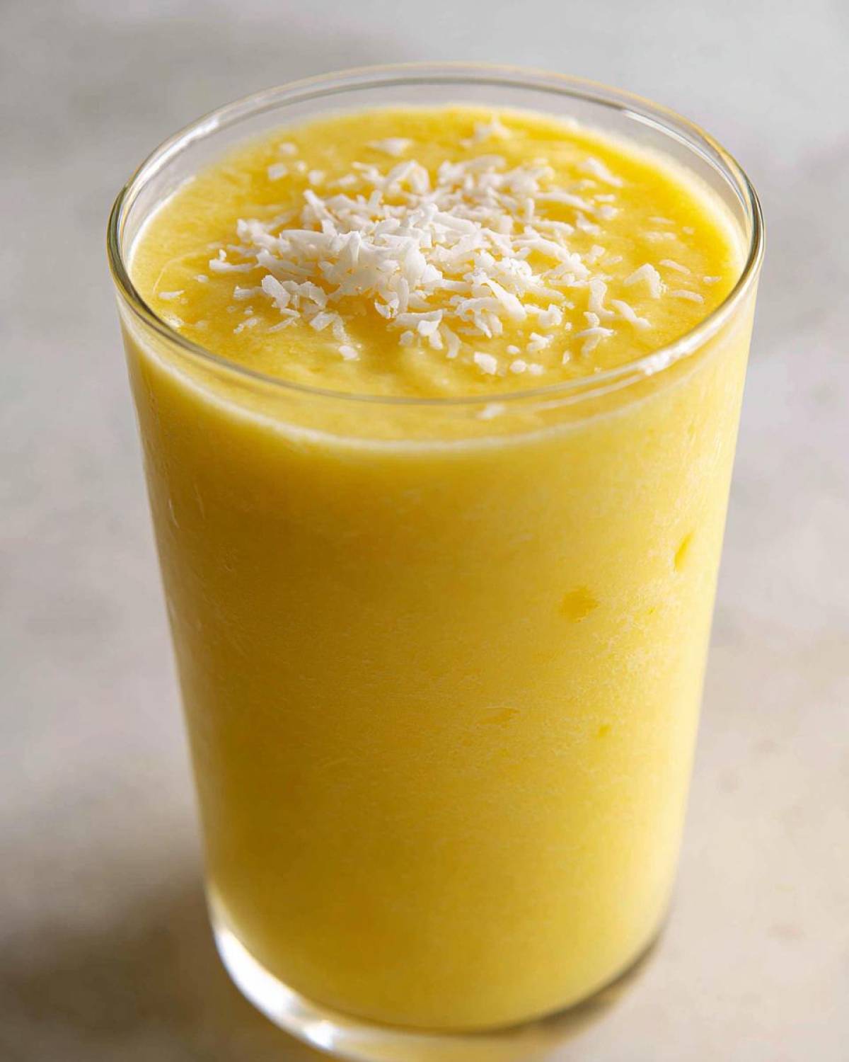 A tall glass filled with a bright yellow Pineapple Coconut Smoothie, topped with shredded coconut.