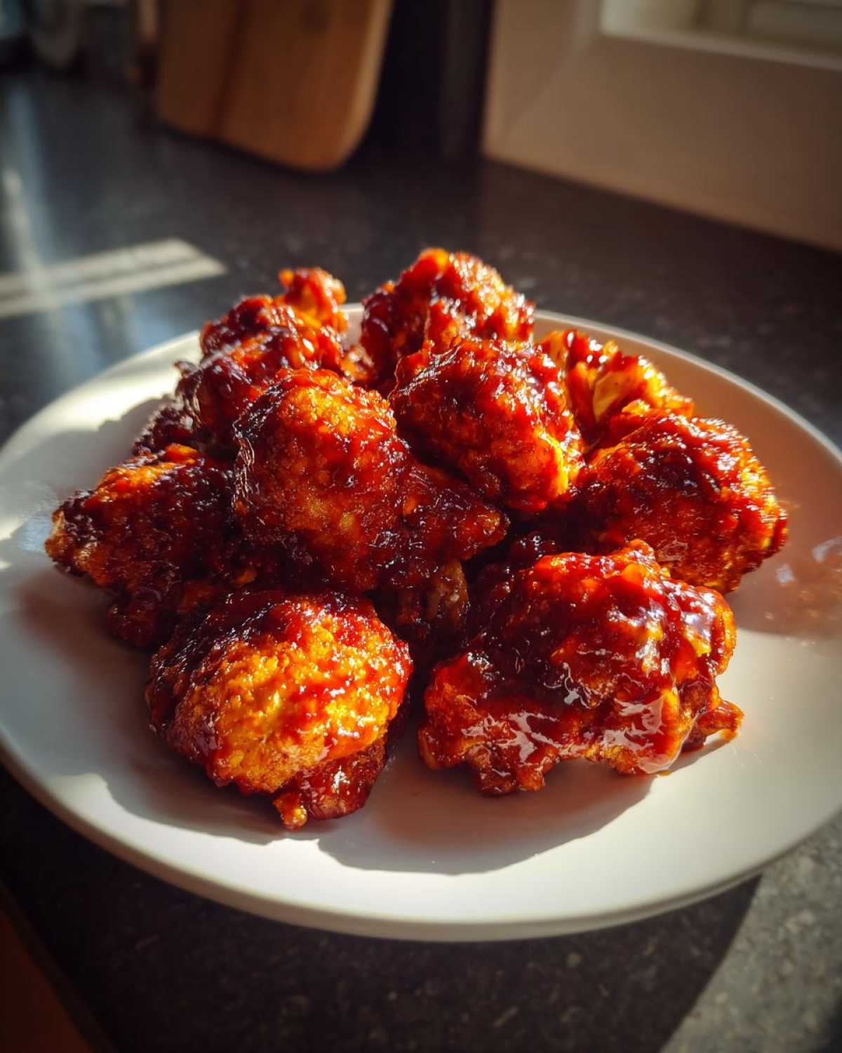 A plate piled high with saucy, glistening Crispy Air Fryer Cauliflower Wings catching the sunlight.