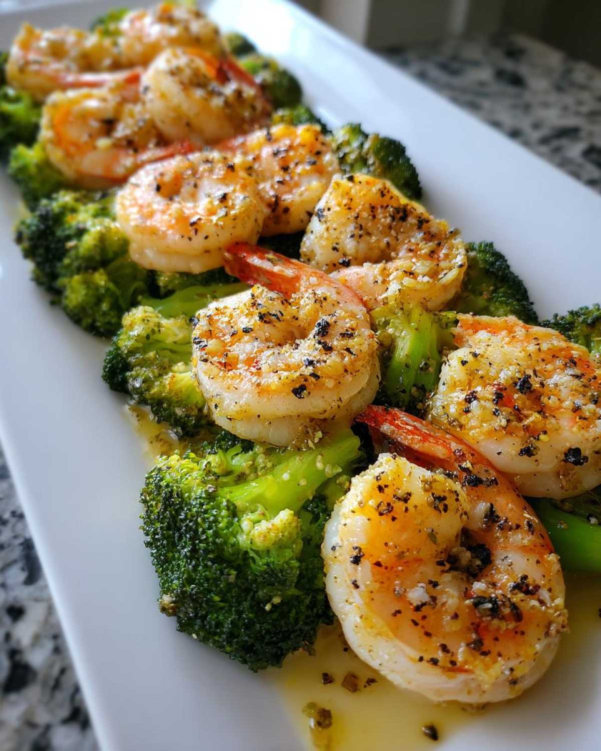 Close-up of perfectly cooked Sheet Pan Garlic Butter Shrimp and Broccoli served on a white platter with garlic butter sauce.