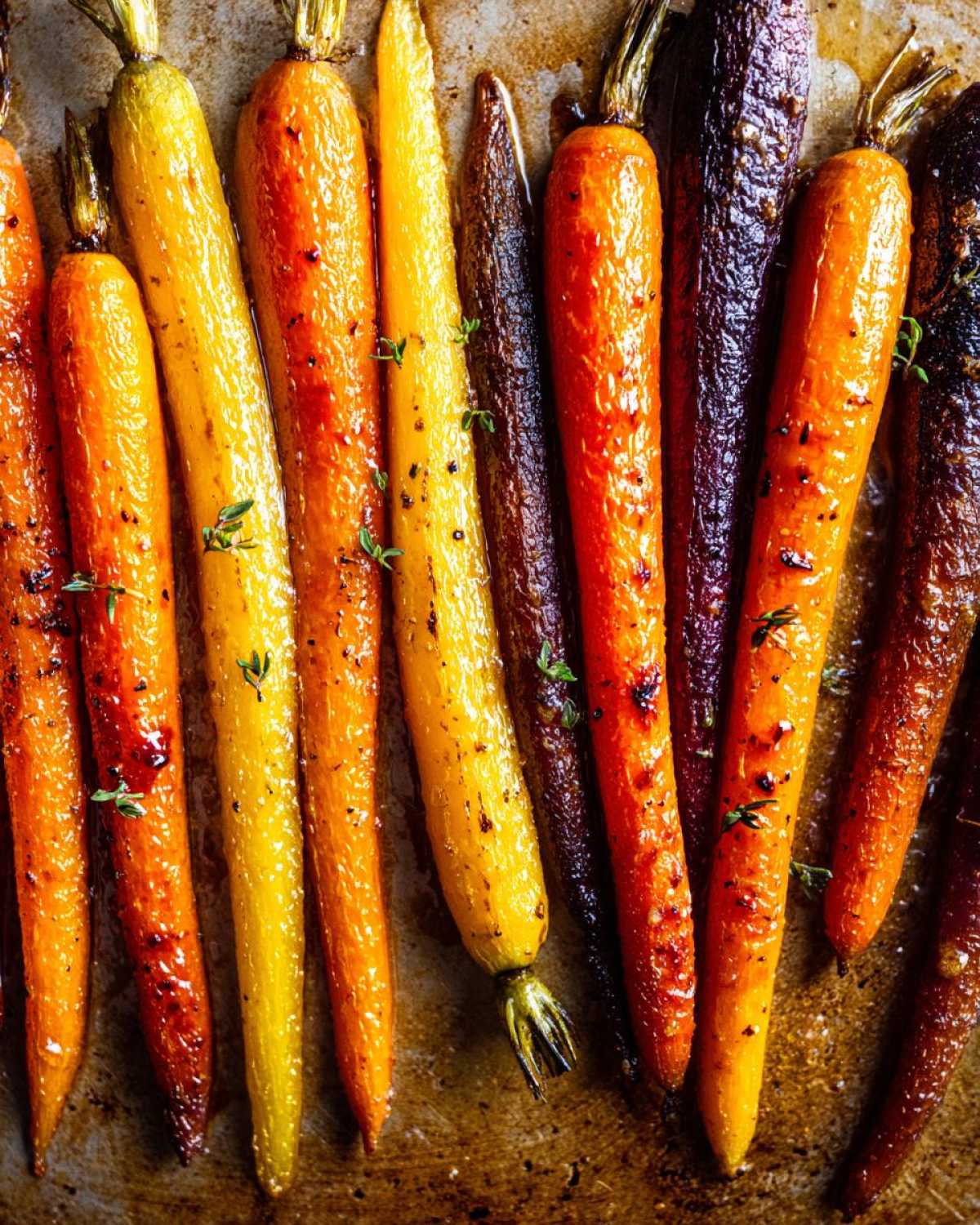 Close-up of glistening, roasted Sheet Pan Roasted Rainbow Carrots with Honey and thyme on a baking sheet.