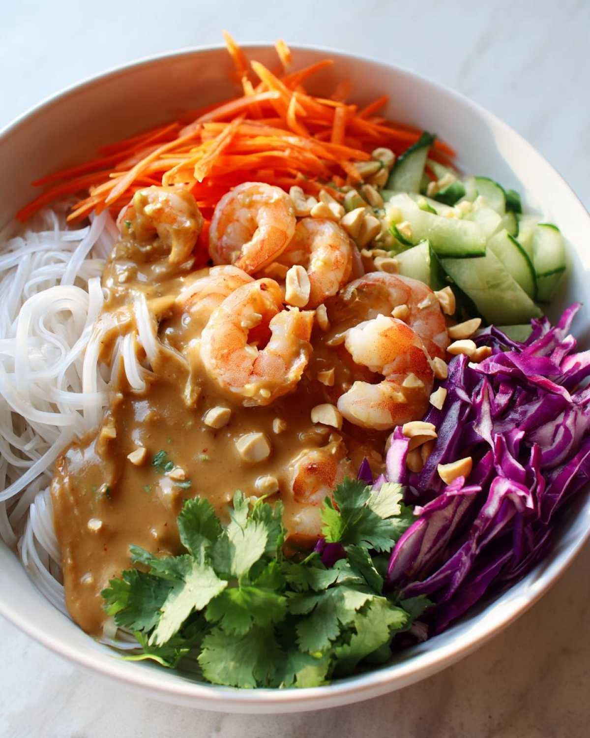 Close-up of a vibrant Spring Roll Bowl with Peanut Sauce, featuring shrimp, rice noodles, shredded carrots, cucumber, and red cabbage.