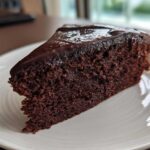A moist slice of rich Gluten-Free Chocolate Cake topped with glossy dark chocolate ganache on a white plate.