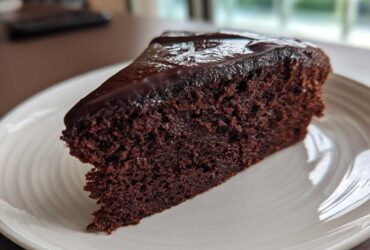 A moist slice of rich Gluten-Free Chocolate Cake topped with glossy dark chocolate ganache on a white plate.